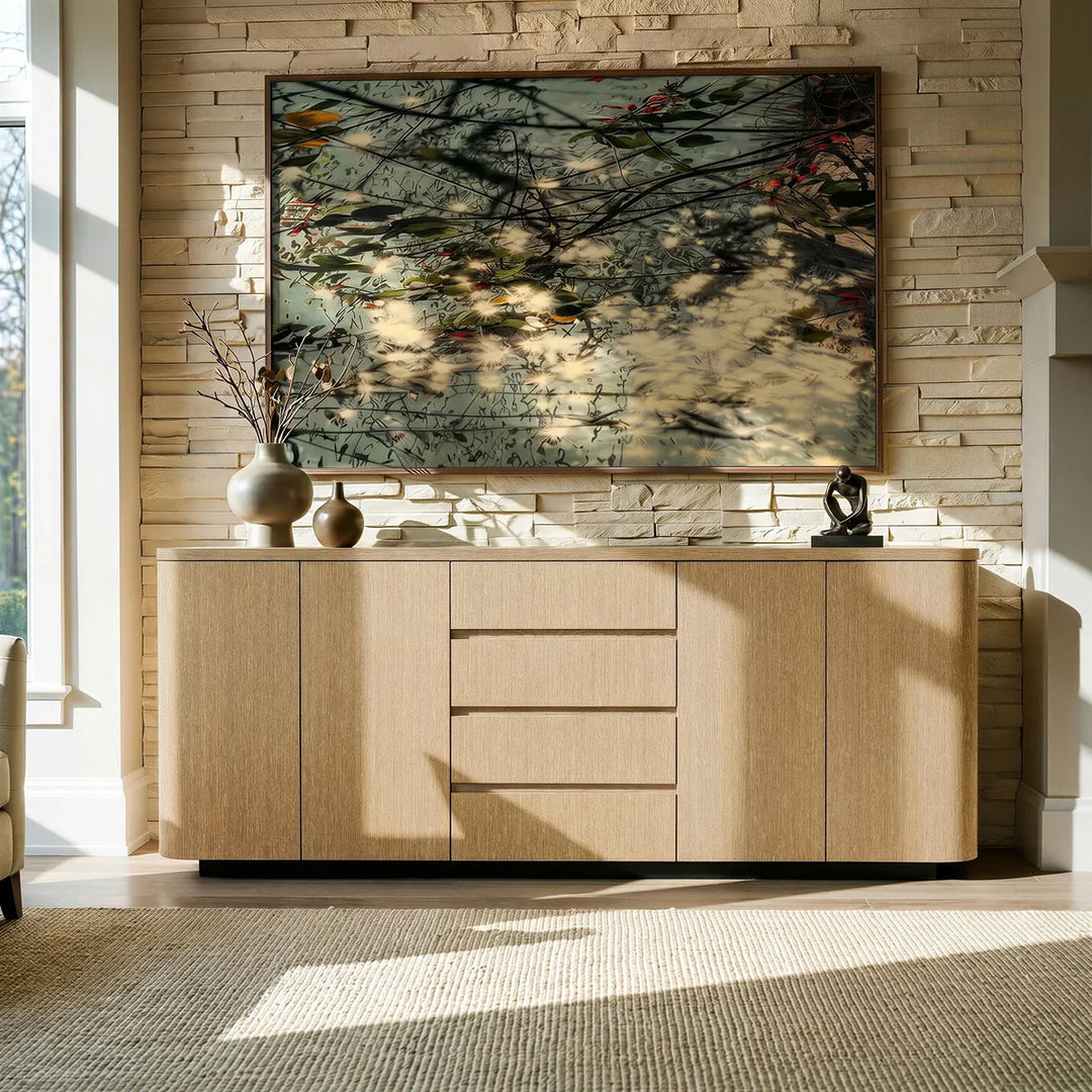 Light oak rounded sideboard below a large painting against a pale stone wall