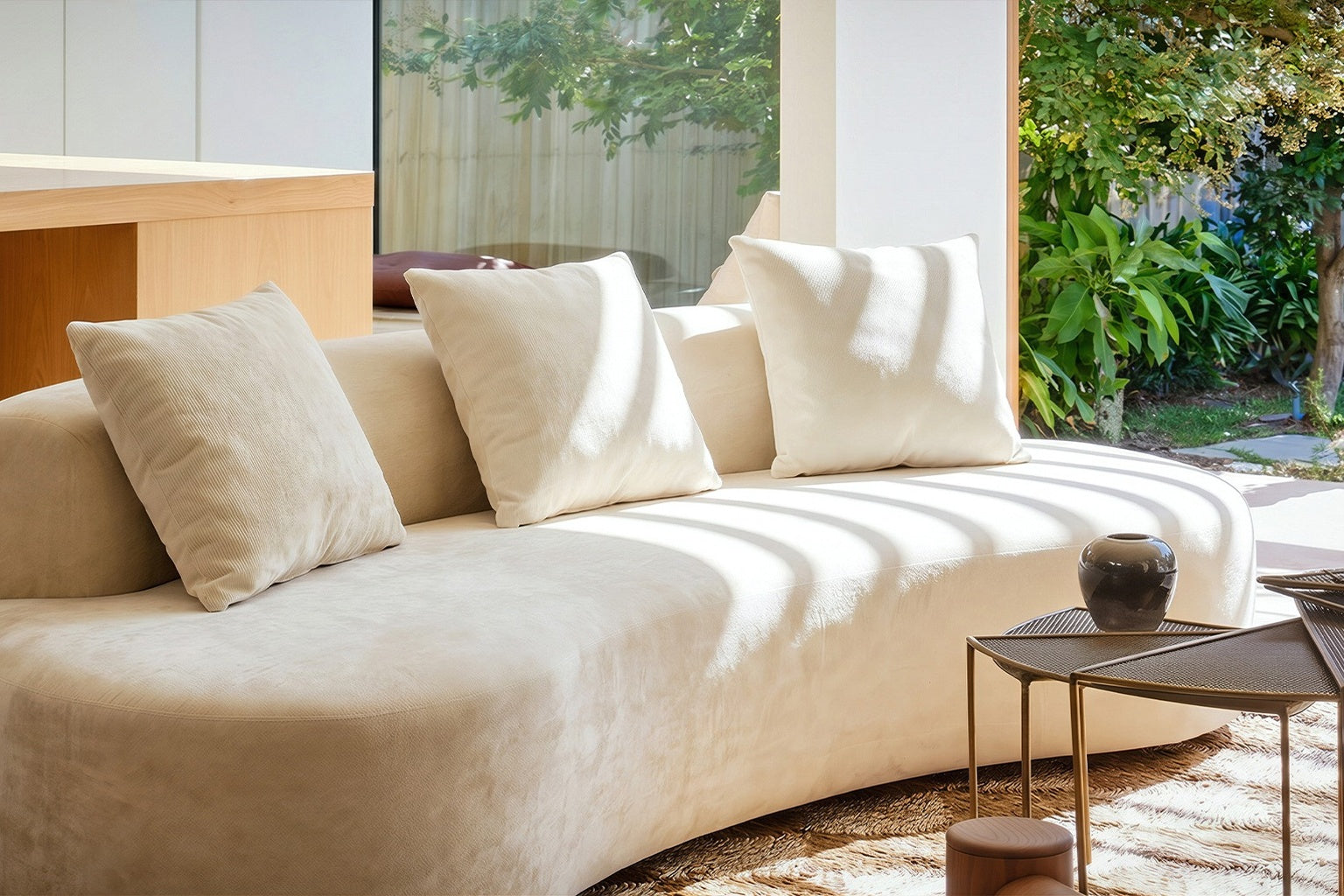 Transitional living room with a curved neutral sofa, warm wood coffee table, layered rugs, and clean architectural lines